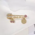 Primo piano dettagliato di una spilla di sicurezza dorata con strass e ciondoli. - Serie Rosa Chiaro