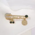 Primo piano dettagliato di una spilla da balia dorata vintage con strass brillanti e ciondoli. - Toni Verde Scuro