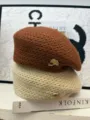 Detailansicht der Strickbarette in Braun und Beige mit schickem Metall-Blatt-Abzeichen. - Karamellbraun