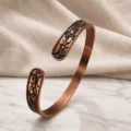 Detailed shot of an open-end copper bracelet featuring vintage floral and scroll engravings. - Antique Color