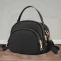 Detail view of black nylon mini shell crossbody bag, featuring gold tone zippers and strap. - Black