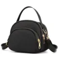 Detailed view of the black nylon mini shell crossbody bag featuring golden zippers and handle. - Black