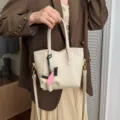 Μινιμαλιστική off-white δερμάτινη τσάντα bucket με χαριτωμένο γούρι πήγασο και λουράκι. - Λευκό του Γάλακτος Με Μενταγιόν Αρκουδάκι
