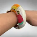 Detailopname van de kleurrijke geemailleerde toucan metalen armand gedragen om de pols. - Bangle / Broken Wit