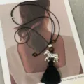 Detailed shot of a long sweater necklace featuring a silver zebra pendant and black tassel. - Black