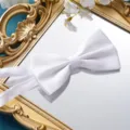 Detaillierte Ansicht einer eleganten weißen Satin-Fliege auf einem goldenen Spiegel für die Hochzeit. - Glatte Weiße Fliege