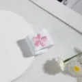 Nahaufnahme von weißem Stoff mit süßer rosa Kirschblütenstickerei, feines Kleidungsdetail. - Blumen Schnalle / Weiß