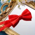 Nahaufnahme einer leuchtend roten Satinfliege auf einem edlen antiken Goldspiegel als Detail. - Glatte Hellrote Fliege