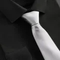 Detail view of a classic silver diagonal textured necktie paired with a black dress shirt. - Silver Fine Striped Zipper Tie