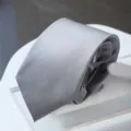Close-up of a sleek grey striped business necktie neatly folded on a white display stand. - Zipper Style / Silver Fine Line