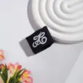Detaillierte Nahaufnahme eines schwarzen JK Uniform Stoffaccessoires mit weißer Stickerei. - Buchstaben Schnalle / Schwarz