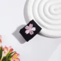 Detailansicht eines schwarzen JK-Uniform-Accessoires mit zarter rosa Kirschblüten-Bestickung. - Blumen Schnalle / Schwarz