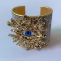Gedetailleerde close-up van een brede gouden armband met boze oog motief en fonkelende strass steentjes. - Stijl B (Goudkleur)
