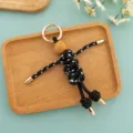 Detailed close-up of the handmade rope-woven doll keychain, featuring wooden head and metal accents. - Black Braided Rope