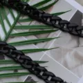 Detailed shot of a black acrylic bag chain, glossy chunky links on green leaves background. - Black