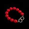 Detailed close-up view of red round bead handbag strap accessory featuring gold metal rings. - Red