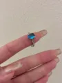 Detail view of a silver ring with an oval blue stone and delicate diamond accents on a finger. - Oval Blue Gemstone Style