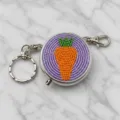 Detaillierte Nahaufnahme einer perlenbesetzten Metall-Pillenbox mit Karottenmotiv. - Karotten-Stil