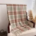 Detailed close-up view of a cozy plaid boucle shawl with tassels displayed on a warm chair. - Light Brown