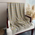 Detail shot of the gray and yellow plaid cashmere-feel scarf draped on a cozy chair. - Yellow Blue