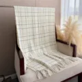 Vue détaillée d'une écharpe à carreaux style cachemire avec franges sur un fauteuil. - Blanc