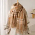 Detailed close-up view of the cozy camel plaid fringed scarf displayed on a nice mannequin. - Camel