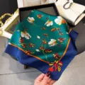 Silk scarf detail view featuring vibrant floral print, green base and contrasting blue border. - Navy Edge