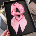 Detailansicht eines rosa Pünktchen-Seidentuchs, elegant geknotet in schwarzer Schachtel. - Rosa