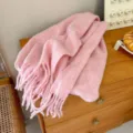Close-up of fluffy pink wool loop yarn winter scarf with fringe detail on wooden table. - Pink