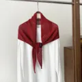 Detail view shot of a red hollow-knit triangular shawl layered over a white long-sleeve top. - 145*42cm / Red
