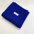 Close-up detail of the folded royal blue knitted scarf featuring a white brand label. - Sapphire Blue / 170cm