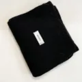 Detailed close-up shot of a cozy black knitted winter scarf, neatly folded with a fabric label. - Black / 170cm