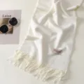 Primo piano dettagliato di una morbida sciarpa bianca con delicate frange ed etichetta. - Bianco puro