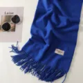 Detail view of a soft royal blue winter scarf featuring elegant fringe and a brand label. - Klein Blue