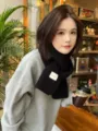 Detail shot of a cozy black knitted winter scarf worn by a model in a cafe setting. - Black