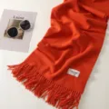 Detailed view of a cozy orange winter scarf with elegant fringe trim and a brand label. - Bright Orange