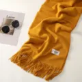 Dettaglio di una sciarpa invernale tinta unita e spessa, con una consistenza morbida e frange. - Giallo