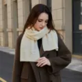 Close-up detail of soft cream knitted scarf worn by model for winter cozy fashion style. - Creamy White / 160