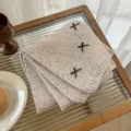 Close-up of cozy knit wool-blend scarf with cute black ribbon cross details on soft oatmeal. - Khaki