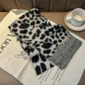 Close-up of black and white leopard print knitted scarf detail on fabric with coffee cup prop. - Dark Gray