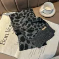 Detailed view of a black and grey leopard print knitted winter scarf displayed on a mat with a coffee cup. - Black