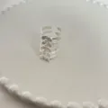 Duidelijke detailopname van een open zilverkleurige metalen ring met unieke wervelvorm. - Zilver