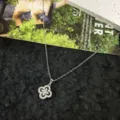 Detail shot of a silver cubic zirconia four leaf clover pendant necklace on black texture. - Rhinestone Clover Necklace