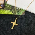 Detailed shot of a delicate gold cross pendant necklace featuring intricate religious relief design. - Style 9