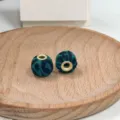 Close-up detail of green leopard print fabric beads with metal eyelets on wood plate. - 14#