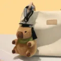 Süßer Wasserschwein Plüschtier Schlüsselanhänger in Braun mit Doktorhut und Schal. - Grünes Halswärmer-Modell