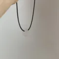 Gedetailleerd overzicht van een minimalistische roze stenen ringketting op zwart koord. - Lichtroze