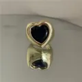 Gros plan détaillé d'une bague cœur massive dorée avec une pierre précieuse bleu foncé. - Anneau Doré Cœur Noir