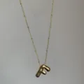 Detailopname van een vergulde ketting met dikke letter F hanger en fijn kraalkettinkje. - Goud F