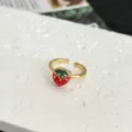 Primo piano dettagliato dell'anello aperto dorato con motivo di fragola in smalto rosso e verde. - Stile Fragola Smaltata Rosso Verde Fascia Liscia (2)
